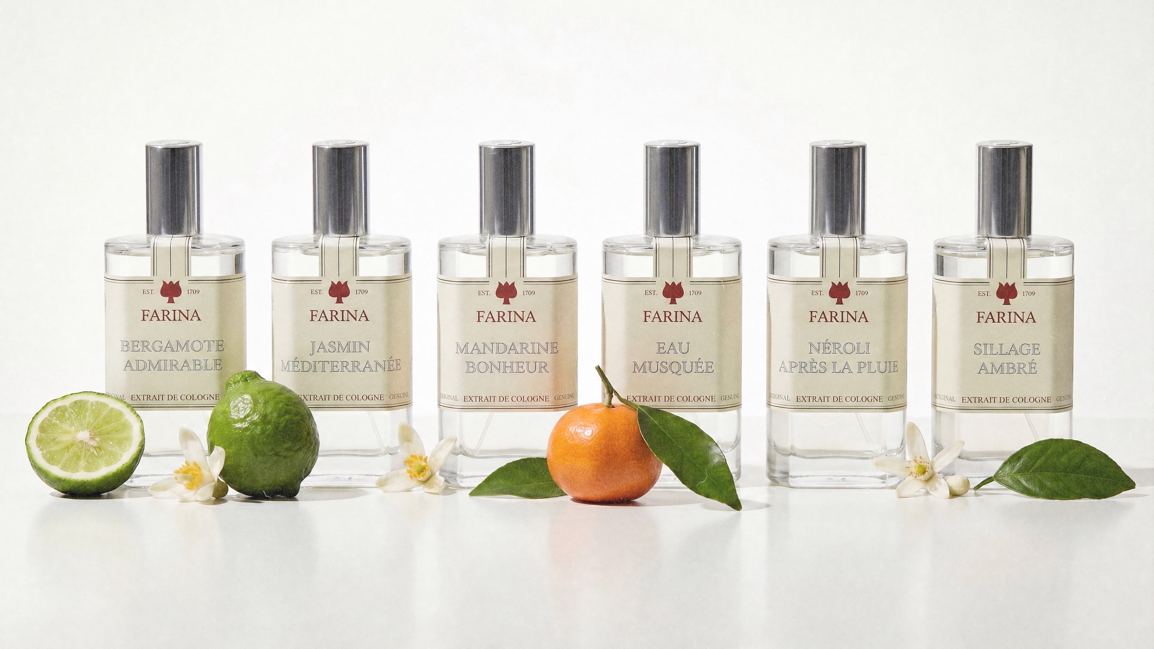 Sechs Farina Extrait de Cologne Flakons in einer Reihe: Bergamote Admirable, Jasmin Méditerranée, Mandarine Bonheur, Eau Musquée, Néroli Après la Pluie und Sillage Ambré, umgeben von Zitrusfrüchten und Blüten