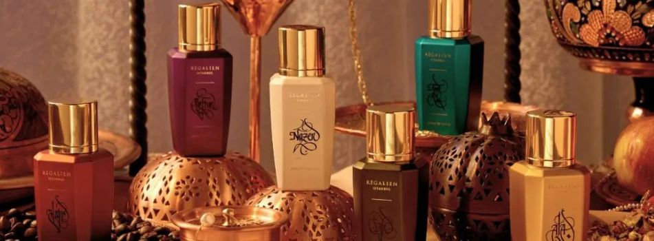 Mehrere luxuriöse Regalien-Parfumflakons in Rot-, Grün- und Cremetönen mit goldenen Verschlüssen, arrangiert auf orientalisch verzierten Metallgefäßen vor warmem, dekorativem Hintergrund.