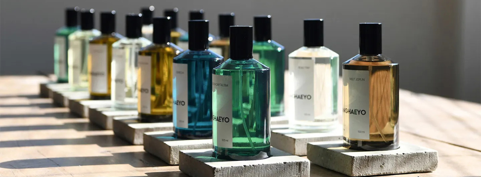Saranghaeyo Eau de Parfum – Kollektion verschiedener Duftflakons in Blau, Grün, Gelb und Braun auf Betonplatten und Holztisch im Sonnenlicht