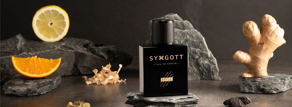 Schwarzer Parfumflakon Syxgott Arise Eau de Parfum steht auf grauen Steinen, umgeben von Orangenscheibe, Zitronenscheibe, Ingwerwurzel und getrockneten Gewürzen vor dunklem Hintergrund.