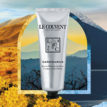 Silberfarbene Tube der Marke Le Couvent mit schwarzem Schraubverschluss. Auf der Tube steht: ‚Gardinarius – Baume Mains du Jardinier – Gardener’s Hand Balm‘. Im Hintergrund ein farbenfrohes Naturmotiv mit Bergen, Blumenfeldern und einem stilisierten Torbogen.
