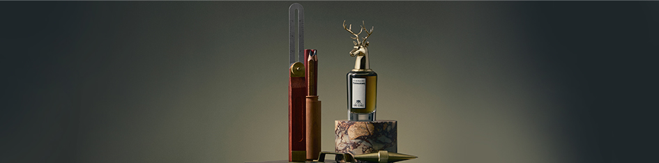 Penhaligon’s Parfum 'The Tragedy of Lord George' aus der Portraits-Kollektion. Der markante Flakon mit goldener Hirschkopf-Kappe steht neben Maßwerkzeugen auf einem Marmorsockel.