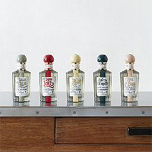 Fünf Parfumflaschen aus der Penhaligon’s Potions & Remedies Kollektion stehen nebeneinander auf einem Holztisch. Die rechteckigen Flakons tragen bunte Verschlusskappen und Etiketten im Apothekenstil.