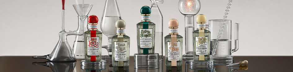 Fünf kunstvoll gestaltete Parfumflakons von Penhaligon’s stehen zwischen gläsernen Laborgeräten in einem alchemistisch wirkenden Aufbau.