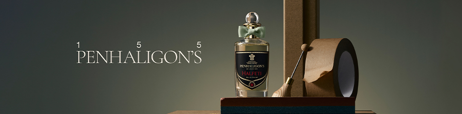 Penhaligon’s Duft 'Halfeti' mit dunklem Etikett und grüner Schleife steht auf einer minimalistischen Szenerie mit Packpapierrolle, Werkzeug und Holzrahmen. Links erscheint das elegante Penhaligon’s Logo mit '155'.