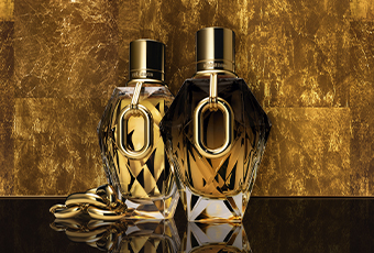 Zwei goldene Parfumflakons von Rabanne Million Gold vor einem glänzenden goldbraunen Hintergrund, links mit einer dekorativen goldenen Kette daneben.